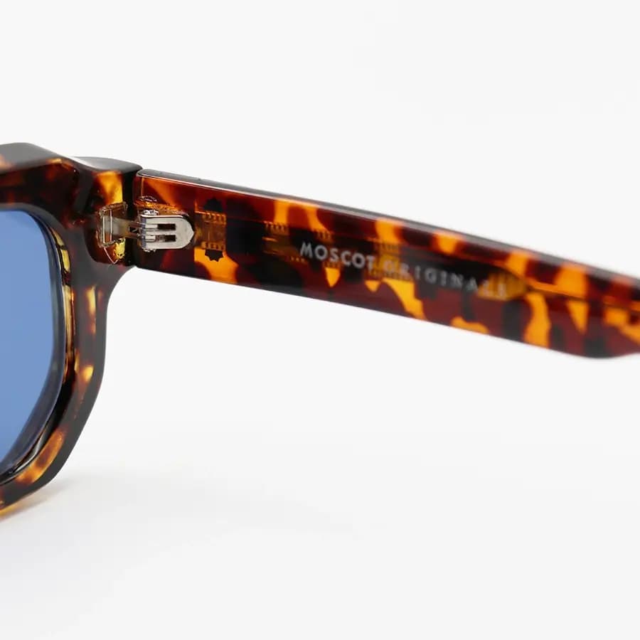 عینک آفتابی MOSCOT با فریم رنگ هاوانا براق، مستطیلی شکل، دسته سیم‌دار و لنز آبی تیره مدل CZ586 — تصویر ۴