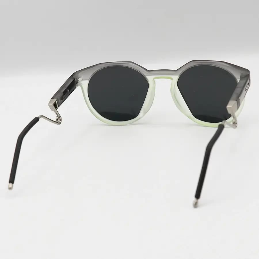 عینک ورزشی OAKLEY با فریم گرد، رنگ طوسی و سبز مات، دسته سنجاقی و لنز دودی تیره و پلاریزه مدل OO9279 — تصویر ۳
